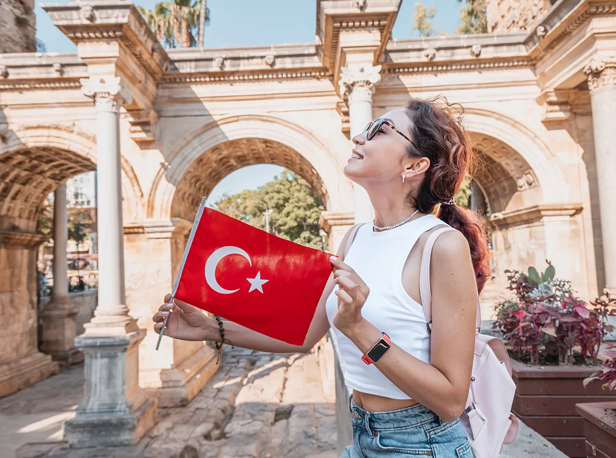 Study in Turkey – Best Universities & Scholarship Opportunities A happy student girl holding the Turkish flag at a historic site, symbolizing academic pride.